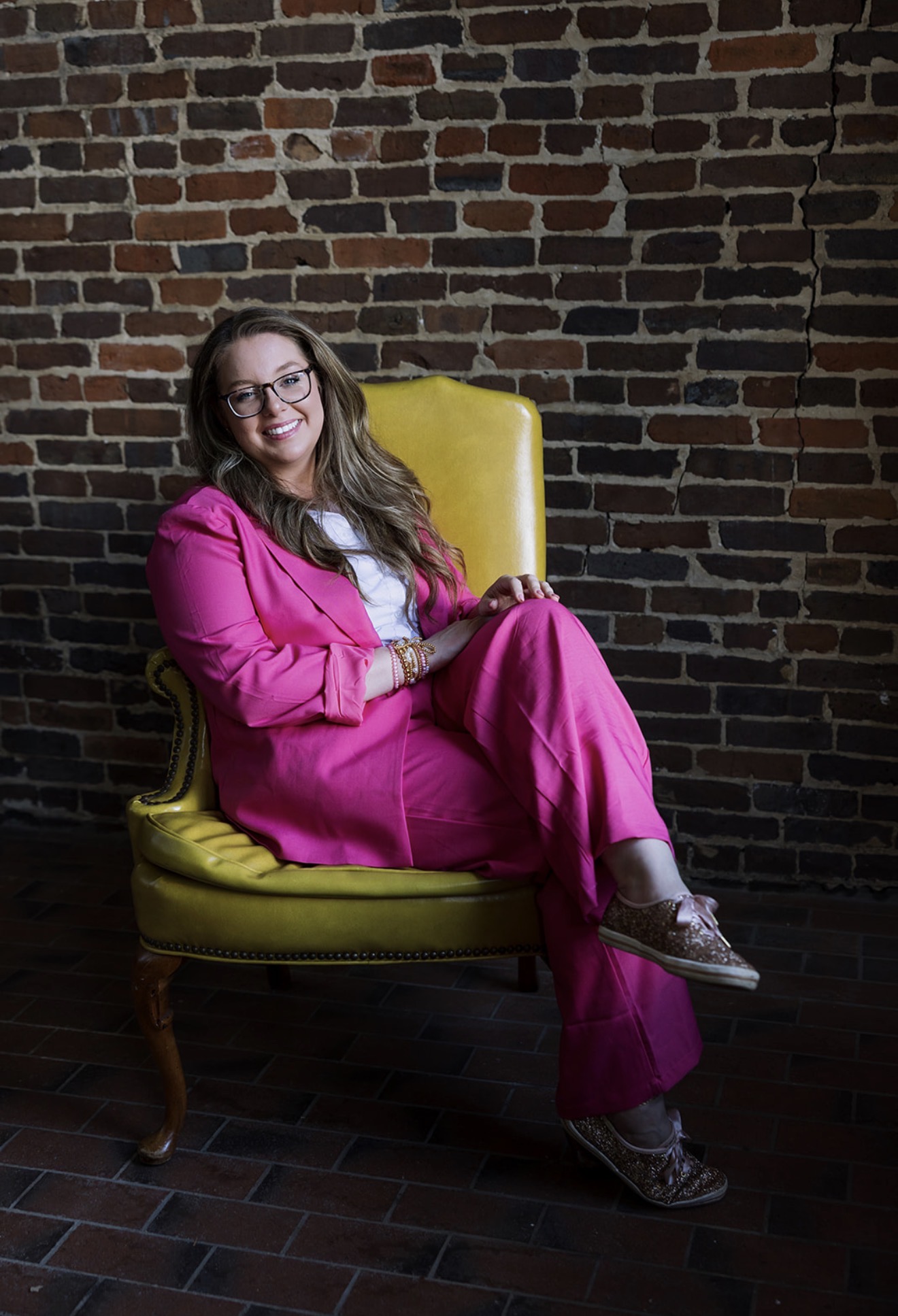 Katie Coleman in a yellow chair against a brick wall